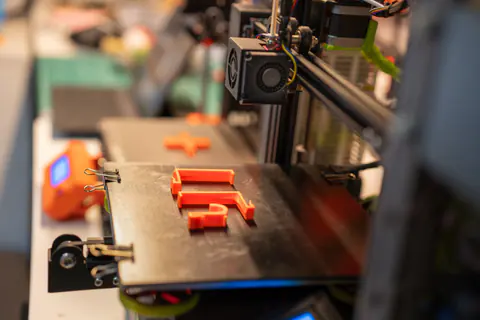 Lotto di pezzi arancioni stampati sul piatto di una stampante 3D